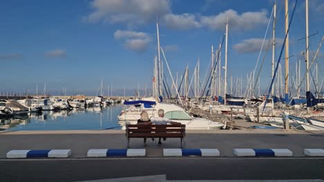 Couple-sitting-on-a-bench-looking-at-the-boats-in-a-quiet-harbor-at-sunset