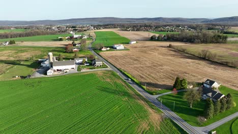 Drone-flyover-farm-house-with-silo-surrounded-by-cultivation-fields-in-american-countryside