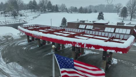 American-and-Pennsylvanian-Flag-waving-in-front-of-closed-gas-station-during-cold-and-snowy-winter-day-in-USA