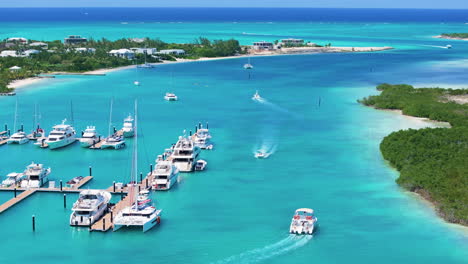 Tilt-up-aerial-4K-footage-of-a-boat-cruising-in-the-blue-waters-of-a-marina,-passing-stationary-yachts-on-the-left