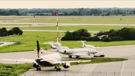 Aviones-Blancos-Empujando-Desde-La-Terminal-Del-Aeropuerto-Cerca-De-La-Pista-Con-Pequeños-Jets-Privados