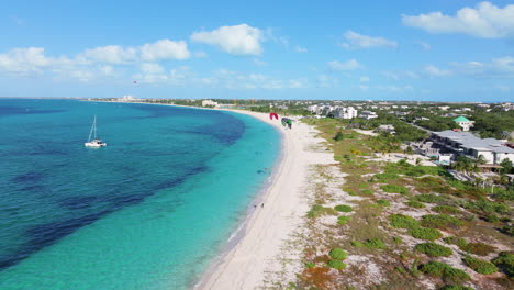 Vorwärts-Luftaufnahmen-In-4K-Von-Der-Küste-Der-Grace-Bay-Mit-Parasailing-Aktivitäten,-Einem-Boot-Auf-Dem-Lebhaften-Blauen-Ozean-Und-Grünem-Land-Auf-Der-Rechten-Seite