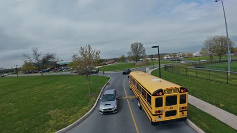Drone-shot-showing-yellow-school-bus-on-road-towards-american-high-school