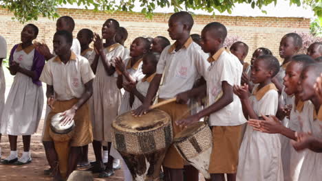 Jóvenes-Estudiantes-Negros-Africanos-Vestidos-Con-Uniforme-Escolar-Tocando-Tambores-Y-Cantando-Mientras-Bailan-Todos-Juntos-Realizando-Un-Ritual-De-Danza-Indígena-Tradicional