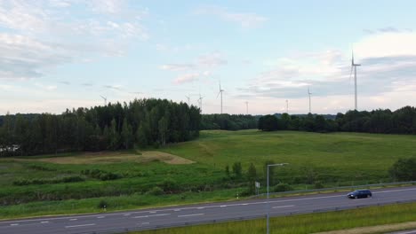 Tall-wind-turbines-standing-above-forest-near-highway-road,-semi-truck-parked