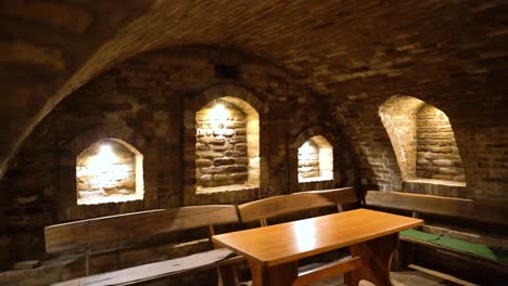 Cozy-rustic-wine-cellar-with-brick-arches,-wooden-benches,-and-a-central-table-illuminated-by-lights