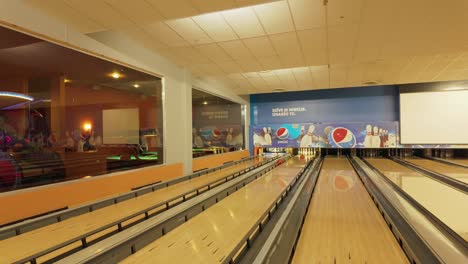 A-child-with-a-braid-eagerly-runs-towards-a-bowling-alley-lane,-enthusiastically-throws-a-ball-amidst-the-vibrant-atmosphere-of-the-bowling-center