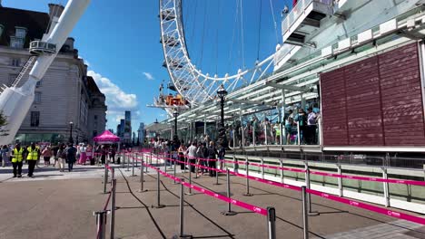 Cola-Vacía-Con-Gente-Haciendo-Cola-Junto-Al-London-Eye-Bajo-Un-Cielo-Soleado,-Destacando-La-Vida-Urbana-Moderna-Y-Las-Actividades-De-Ocio-En-Un-Ambiente-Vibrante