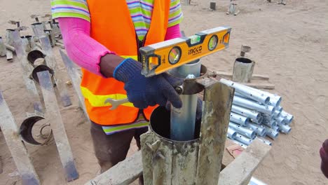 Cerrar-Las-Manos-De-Un-Técnico-Africano-Nivelando-Y-Ajustando-El-Molde-Del-Marco-Del-Pilote-De-Hormigón-Y-El-Soporte-Para-El-Pilote-De-Hormigón-Solar-Fotovoltaico.