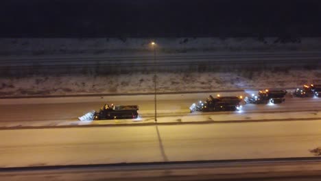 Drone-moves-from-above-with-trucks-clearing-snow-from-road-with-sirens-on-during-night