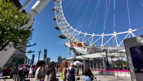 Visitors-gather-and-queue-at-the-London-Eye,-a-popular-attraction-in-London,-under-a-clear,-sunny-sky