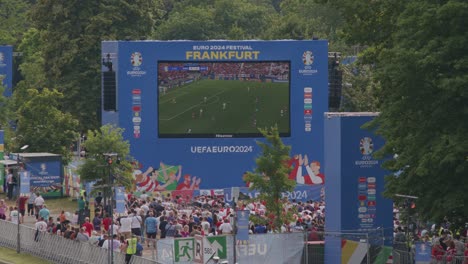 Rückansicht-Von-Fans-Und-Einheimischen,-Die-Sich-Die-Spiele-Der-Europameisterschaft-2024-Im-Fanpark-Am-Mainufer-In-Deutschland-Ansehen