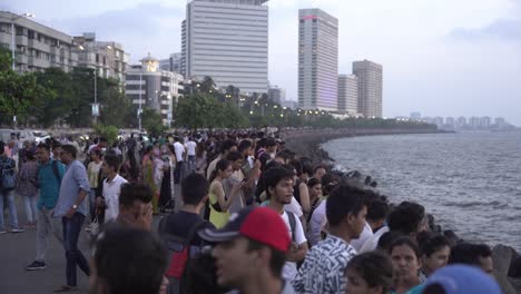 Crowd-of-tourists-enjoying-sunset-on-weekend-at-Mumbai-iconic-landmark-Marine-Drive-beach-with-skyline-buildings-in-background