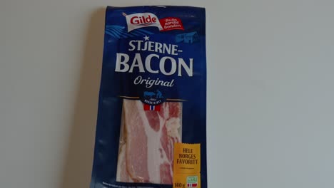 Approaching-view-of-store-bought-Gilde-bacon-pack-on-white-surface,-ending-in-closeup-of-logo-and-name