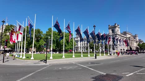 Parliament-Square-Gardens-in-Westminster-adorned-with-Commonwealth-flags-on-a-sunny-day,-with-a-clear-blue-sky-and-an-iconic-historic-building-in-the-background