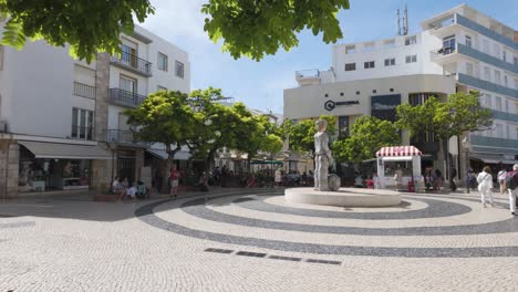 Día-Soleado-En-La-Praça-Gil-Eane-En-Lagos,-Portugal,-Con-Gente-Disfrutando-De-La-Plaza-Y-La-Estatua.