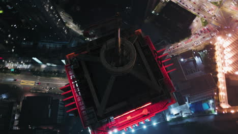 Aerial-view-around-the-top-of-the-illuminated-AM-bank-tower,-night-in-Kuala-Lumpur