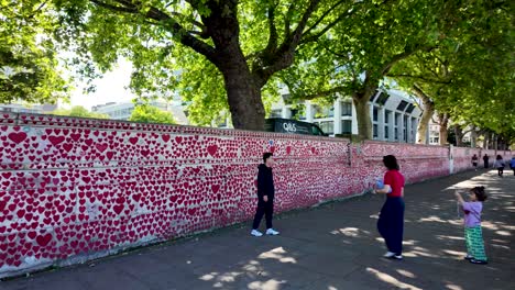 Tourists-admire-the-National-Covid-Memorial-Wall-in-Westminster,-surrounded-by-a-lush-green-environment-and-beautiful-heart-murals-on-a-sunny-day