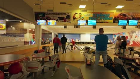 Das-Filmmaterial-Zeigt-Erwachsene-Und-Kinder,-Die-Sich-In-Einem-Bowlingcenter-Vergnügen,-Während-Auf-Fernsehbildschirmen-Ergebnisse-Und-Unterhaltung-Angezeigt-Werden-Und-So-Eine-Lebhafte-Atmosphäre-Entsteht