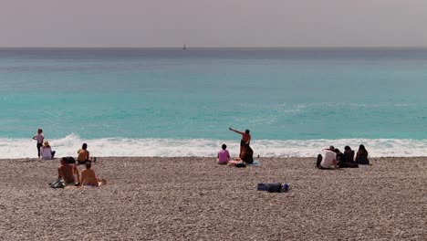 People-relax-on-pebble-beach-in-Nice,-France-with-turquoise-waters-and-calm-atmosphere