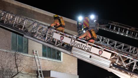 Two-firefighters-climb-truck's-ladders-to-go-into-the-building-to-help-people-during-night