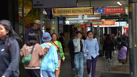 People-strolling-along-the-sidewalk-on-Swanston-St-near-Chinatown,-in-between-Little-Bourke-and-Bourke-streets,-lined-with-shops-and-business-in-Melbourne's-bustling-Central-Business-District