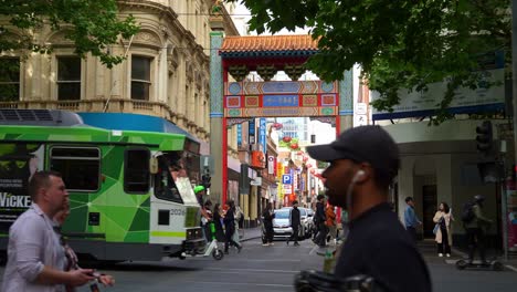 Bustling-downtown-Melbourne-city-featuring-iconic-landmark-gate-of-Chinatown-on-Little-Bourke-street-with-pedestrians-crossing-and-trams-running-along-Swanston-street,-slow-motion-shot-of-street-scene