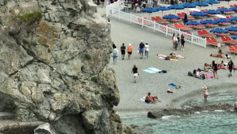 Turistas-En-La-Playa-De-Monterosso-Al-Mare,-Italia,-Con-Un-Vídeo-De-Drones-De-Cerca-Moviéndose-Hacia-La-Estatua-De-Il-Gigante