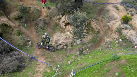 Drohnenflug-über-Eine-Motocross-Strecke-Im-Freien,-Auf-Der-Eine-Meisterschaft-Ausgetragen-Wird.-Wir-Sehen-Einen-Piloten,-Der-Mit-Seinem-Motorrad-Auftritt,-Und-Sein-Berater-Ist-Bei-Ihm,-Und-Zuschauer-Erscheinen-Bei-Der-Veranstaltung