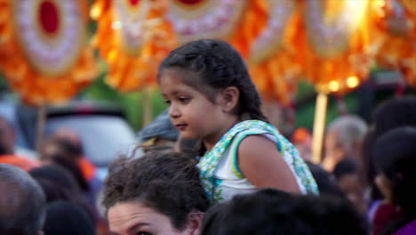 A-little-girl-sits-atop-her-mother's-shoulders-at-a-religious-festival