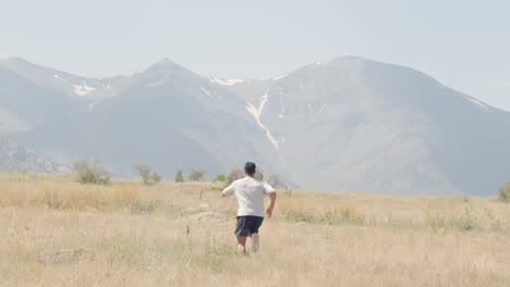 Joyful-runner-races-across-rugged,-dry-terrain-and-jumps,-framed-by-distant-mountains