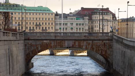 Alte-Steinbrücke-Norrbro-über-Fließendes-Wasser-In-Stockholm,-Schweden,-Grand-Hotel-Im-Hintergrund,-Breite-Statische-Aufnahme