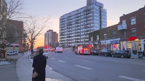 Fire-truck-rushes-at-Montreal-streets-with-its-sirens-on-for-emergency,-Woman-walking-and-city-buildings-in-background