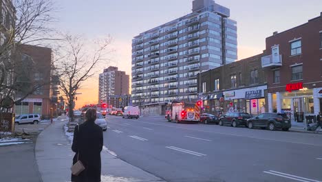 Un-Camión-De-Bomberos-Corre-Por-Las-Calles-De-Montreal-Con-Sus-Sirenas-Encendidas-Para-Emergencias,-Una-Mujer-Caminando-Y-Los-Edificios-De-La-Ciudad-Al-Fondo