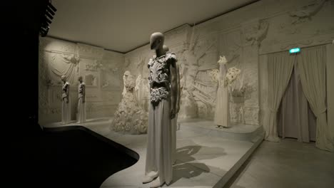 Fashion-exhibition-presenting-various-white-designer-clothes-on-mannequins-in-a-room-decorated-with-ornate-white-moldings