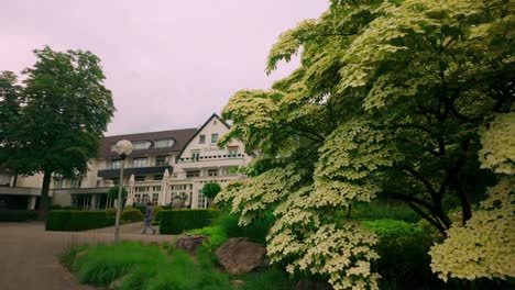 Footage-dollying-to-the-left-of-the-Hotel-Bilderberg-facade,-framed-by-blooming-flowers-and-lush-green-trees