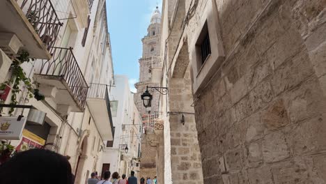 Walking-on-the-Narrow-Streets-of-Monopoli-with-the-Cathedral-in-the-Background,-Bari,-Italy