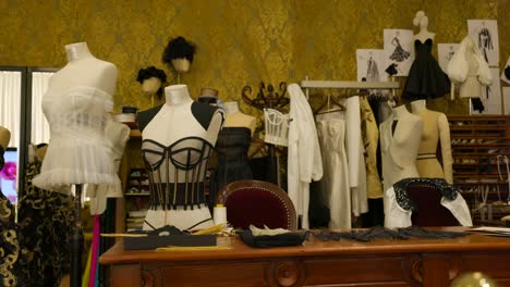 Mannequins-showcasing-various-outfits-including-corsets-and-dresses,-positioned-in-an-intricately-decorated-fashion-design-studio-with-sketches-and-sewing-materials-around