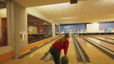 A-woman-with-a-ponytail,-wearing-a-red-sweater,-determinedly-throws-a-bowling-ball-down-the-lane-at-a-bowling-alley