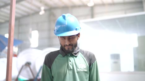 Pakistani-worker-stands-in-a-production-hall-for-textiles-and-smiles-into-the-camera-he-is-wearing-work-clothes-and-a-blue-helmet