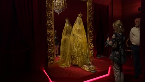 Tourists-photographing-a-golden-dress-exhibited-inside-a-luxurious-room-at-the-palazzo-reale-in-milan,-italy