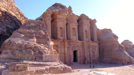 Scenic-view-of-The-Monastery-Ed-Deir-building-carved-into-mountains-with-tourist-visiting-the-ancient-city-of-Petra-in-Jordan