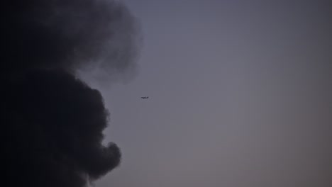 An-aeroplane-flying-and-vanishing-into-the-dark-smoke-from-a-fire