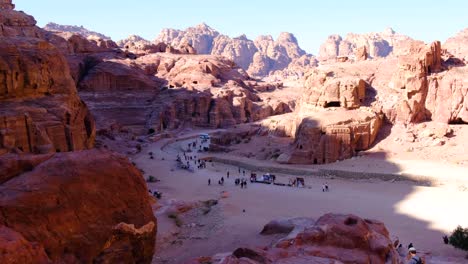 Elevated-view-overlooking-the-ancient-city-of-Petra-with-buildings-carved-into-mountains,-streets-with-market-stalls-and-people-visiting-in-Jordan