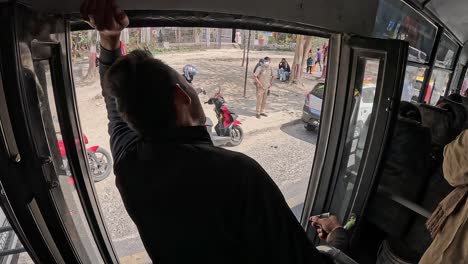 A-Nepalese-bus-ticket-inspector-stands-in-the-open-door,-urging-passengers-to-board-amidst-the-hustle-and-bustle-of-daily-life-in-Kathmandu