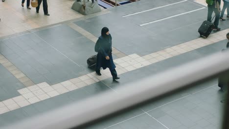 Woman-in-hijab-walking-through-a-train-station,-a-bustling-background-with-people-and-suitcases