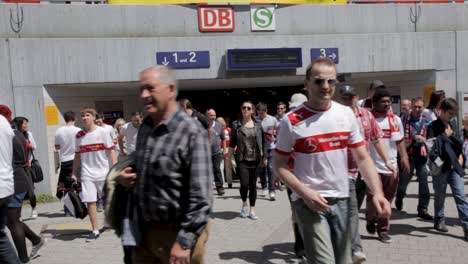 Football-fans-exit-a-station-on-a-sunny-day,-jerseys-displayed,-crowd-dynamic,-urban-setting