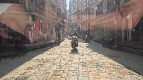 Backseat-view-of-a-car-navigating-the-lively-alleys-of-central-Kathmandu,-following-motorbikers-in-a-dynamic-urban-commute