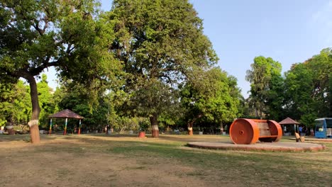 The-camera-pans-from-left-to-right,-showing-a-wide-view-of-the-park-with-grass,-trees,-and-a-uniquely-shaped-bench