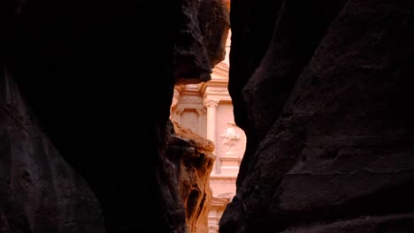 A-glimpse-of-The-Treasury-Al-Khazneh-iconic-Nabatean-building-seen-through-the-narrow-Siq-Trail-pathway-in-ancient-city-of-Petra,-Jordan